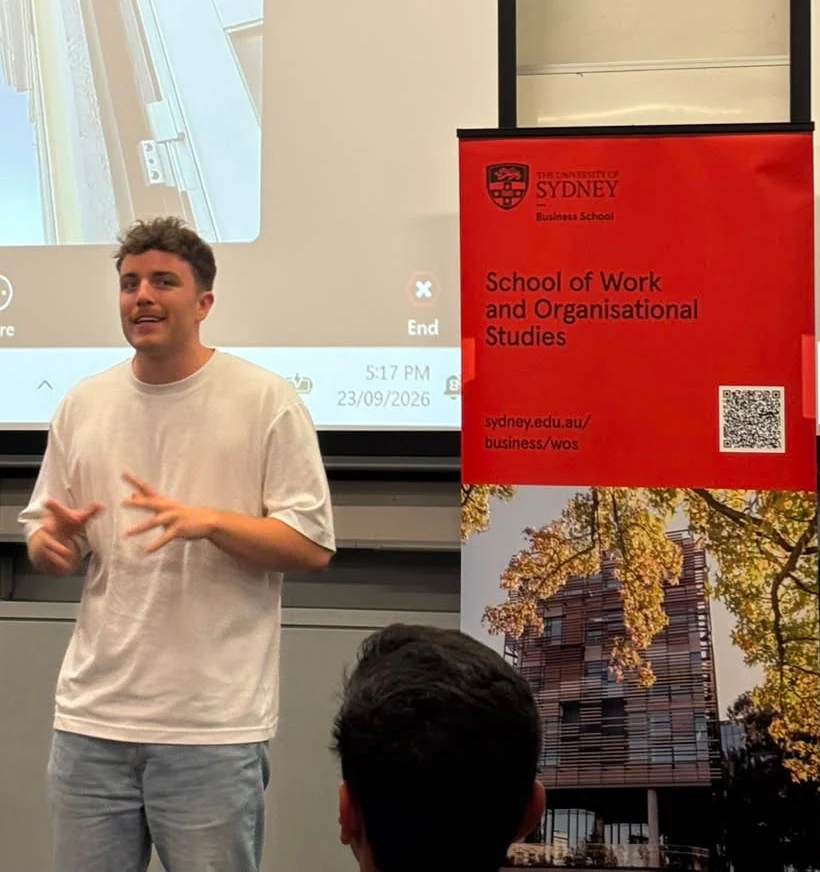 Joseph speaking in front of a University of Sydney Business School banner